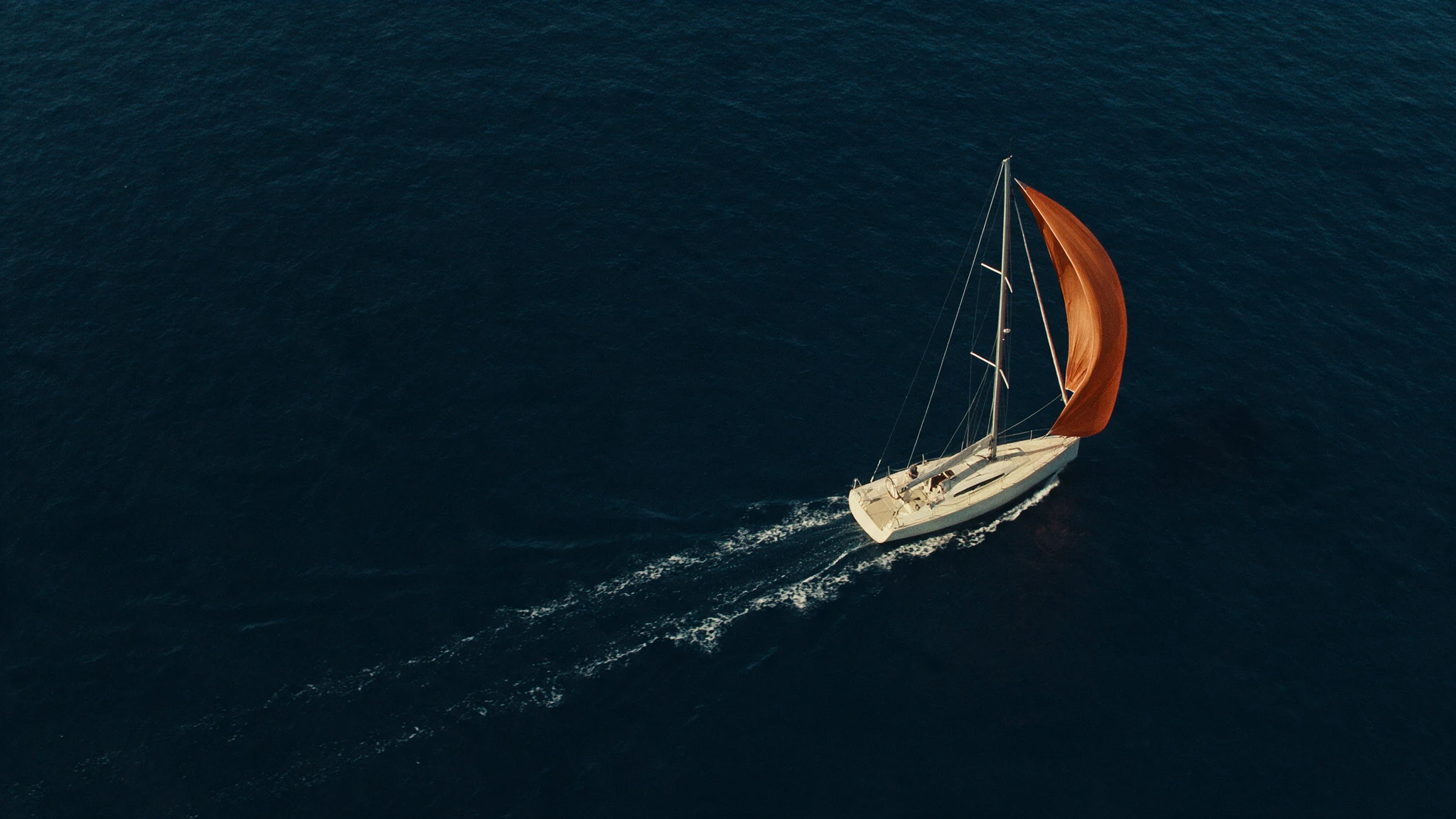 Un velero de vela naranja mantiene un rumbo claro sobre aguas azul profundo
