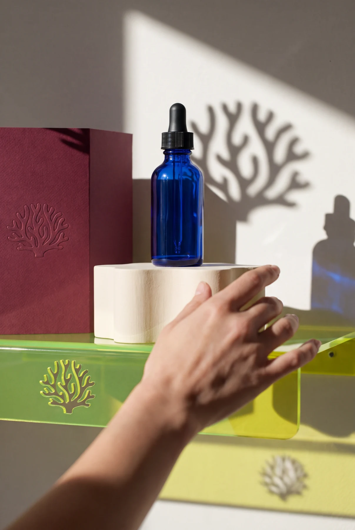 Un producto de vidrio azul comparte motivos físicos entre papel burdeos, acrílico verde y luz natural