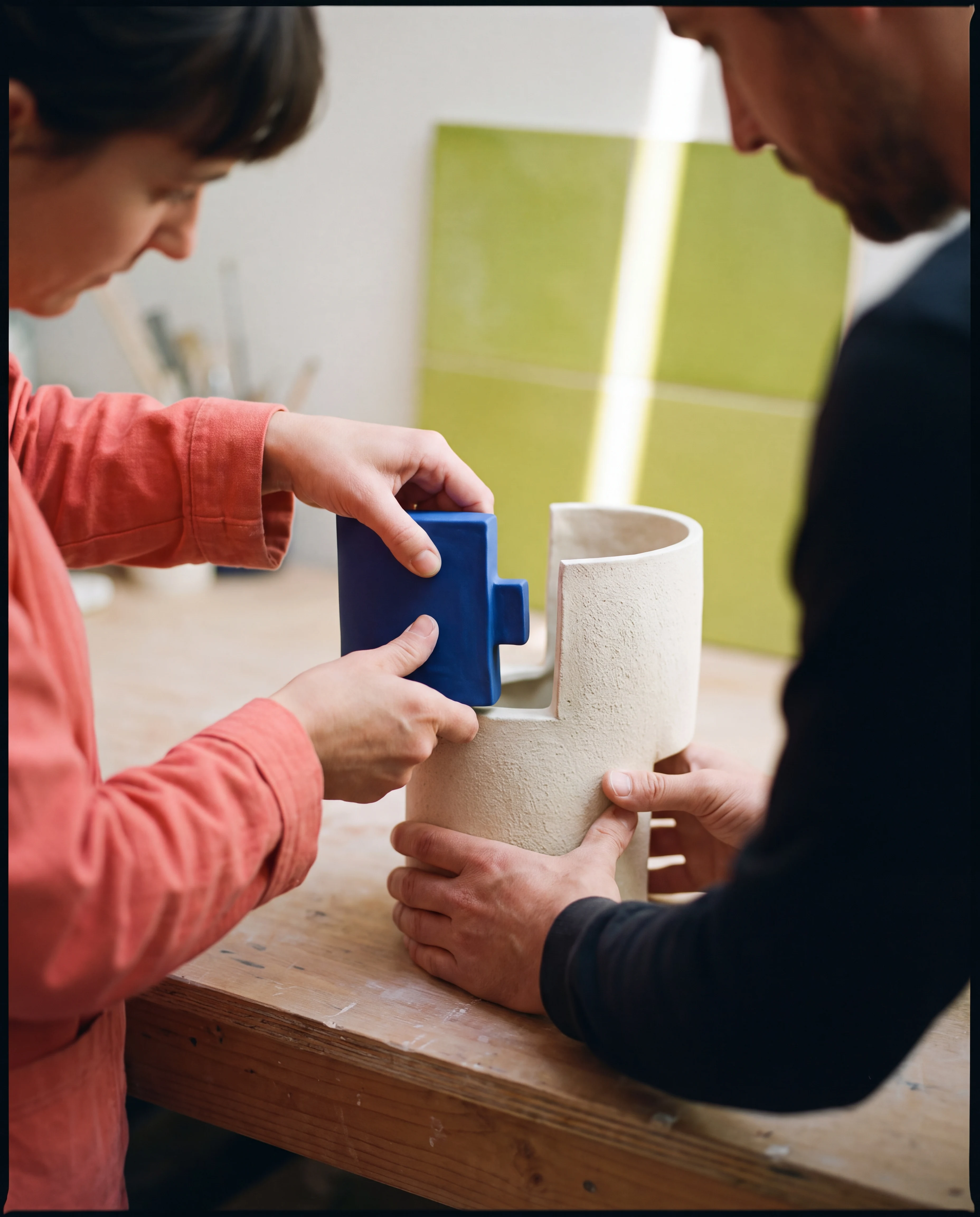 Dos personas ensamblan una pieza modular de cerámica azul sobre una mesa de taller